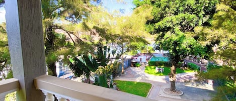 A balcony with a view of a garden, a paved area, and a parked car.