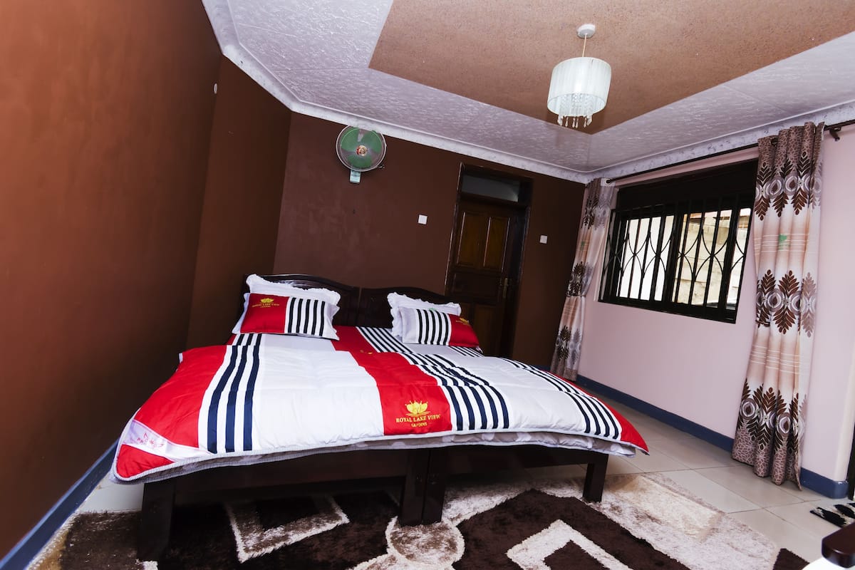 A bedroom with a bed, a ceiling fan, a window with curtains, and a door.