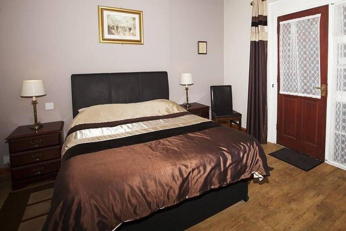 A bedroom with a bed, two bedside tables, a chair, a door with curtains, and a framed picture on the wall.