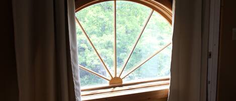 A room with a large arched window, wooden flooring, and a curtain rod.