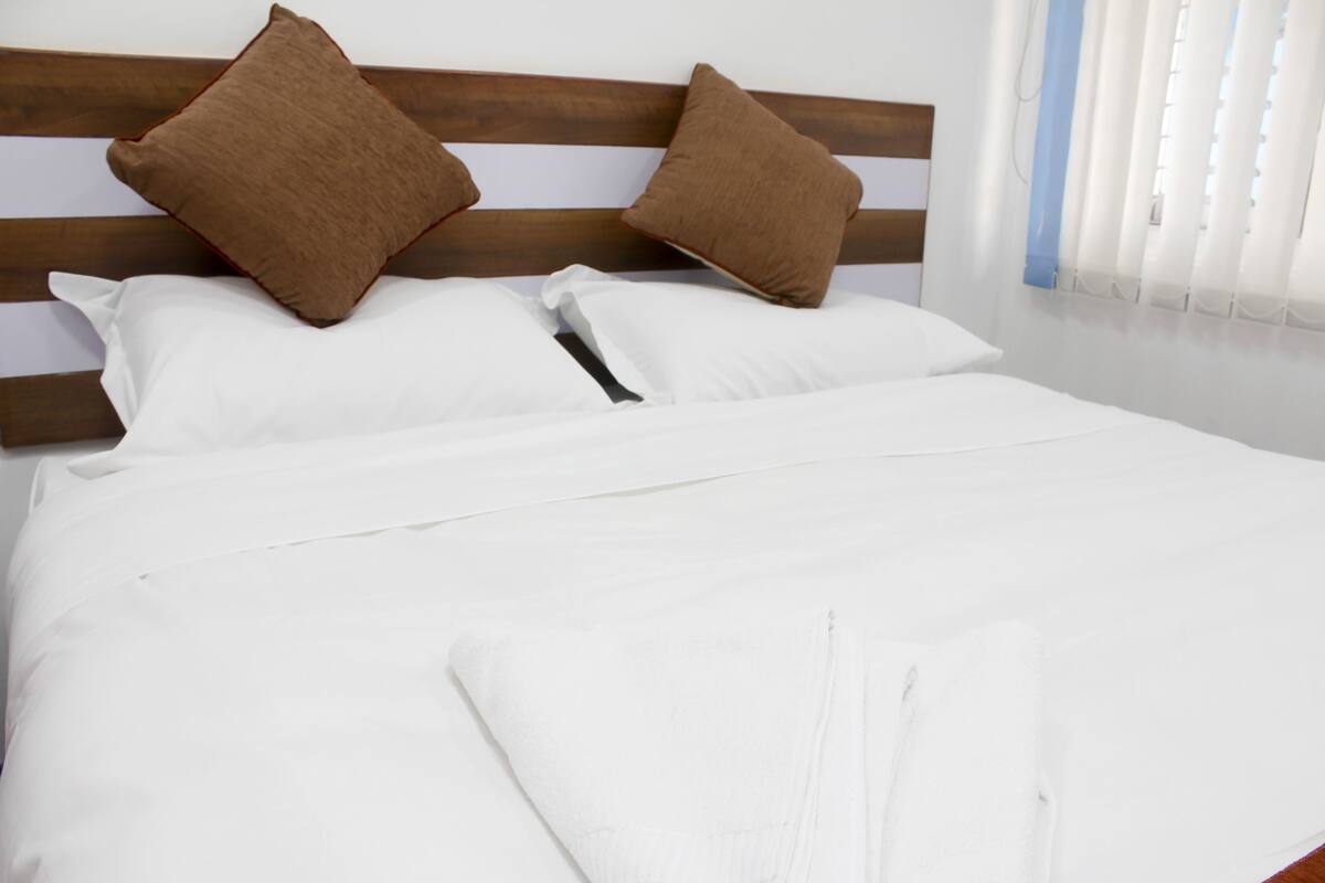 Una cama bien tendida con sábanas blancas y dos almohadas marrones sobre un cabecero de madera.