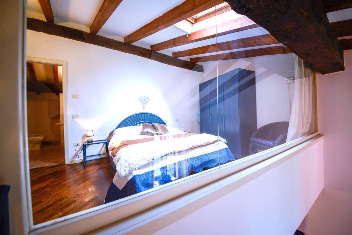 A bedroom with a bed, a nightstand, a window, and wooden beams on the ceiling.
