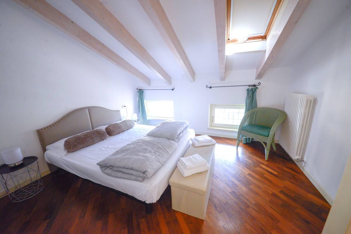 A bedroom with a bed, a bedside table, a radiator, and a window with curtains.