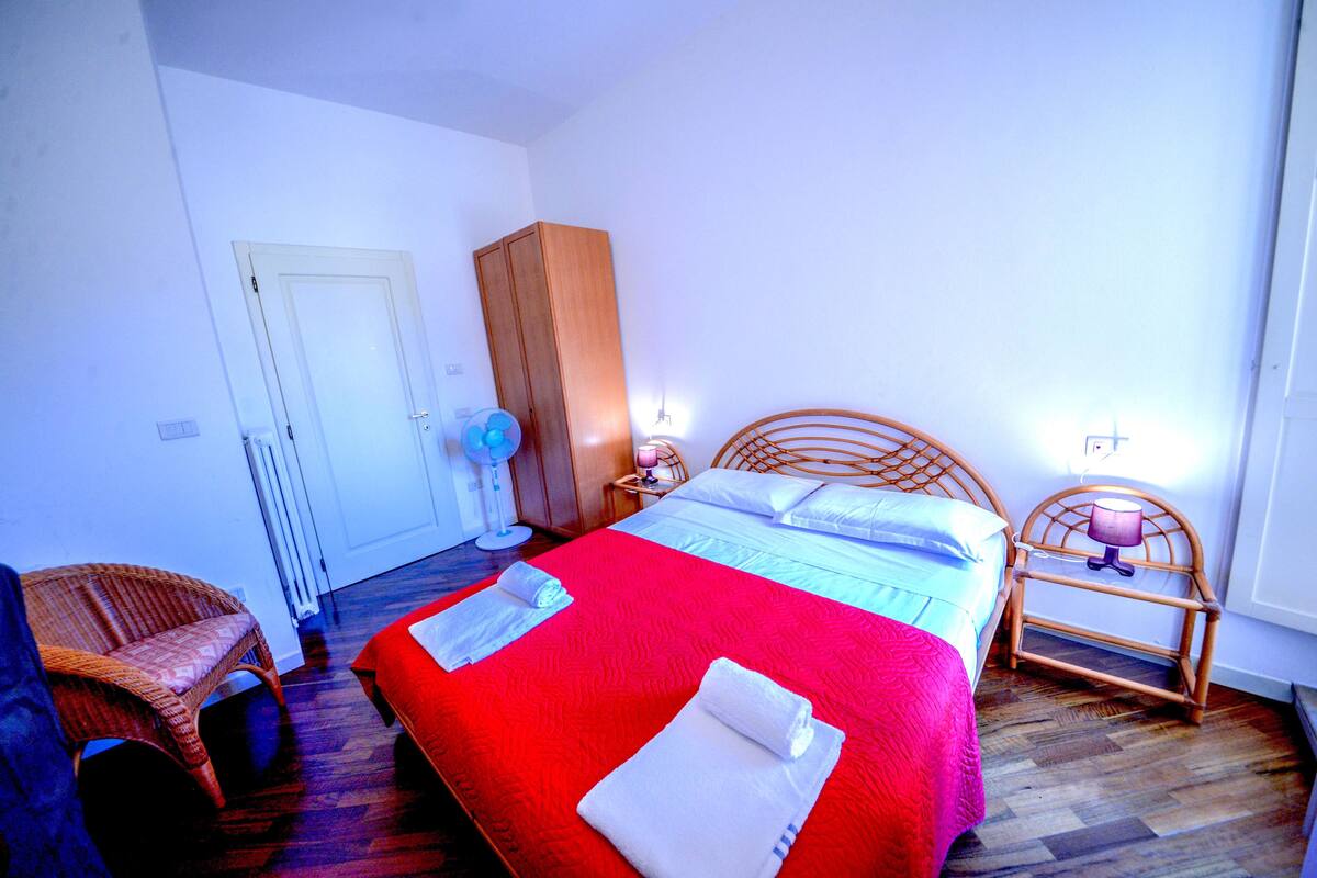 A bedroom with a bed, a chair, a wardrobe, and a bedside table with a lamp.