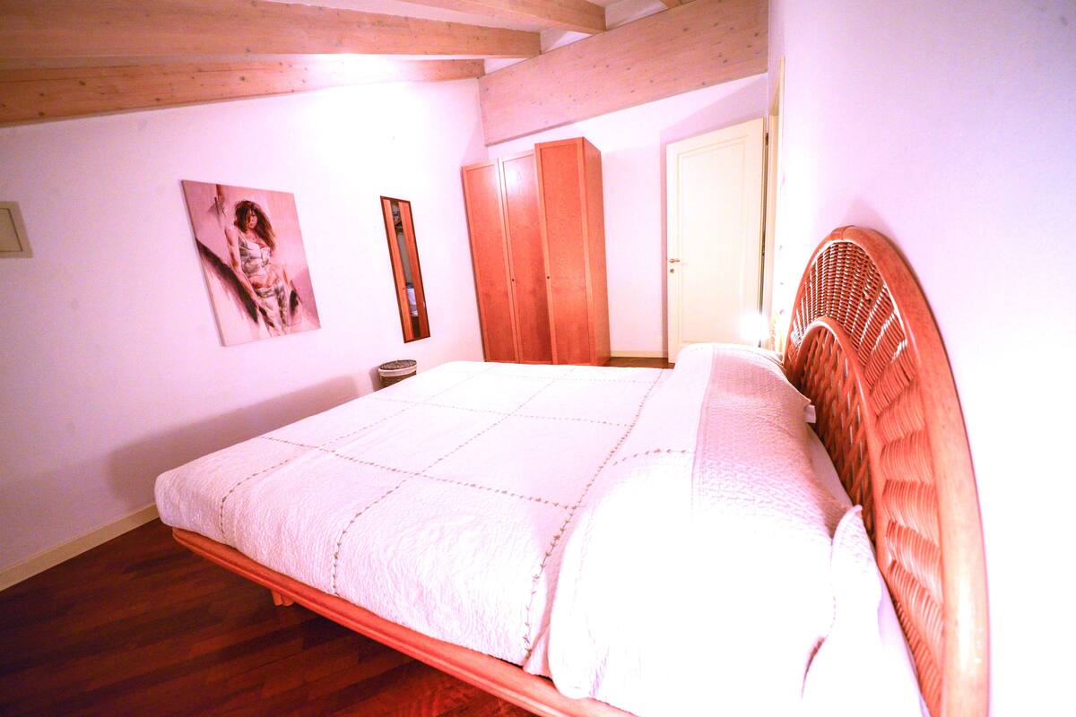 A bedroom with a wooden bed frame, a white quilt, a wooden wardrobe, and a framed picture on the wall.