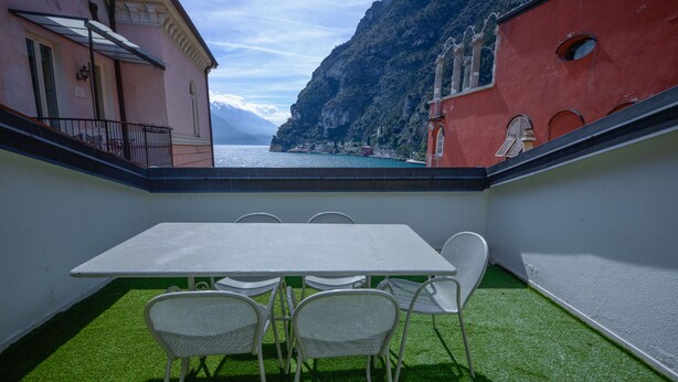 A balcony with a table and chairs, overlooking a mountainous coastline. - Queen of the Lake (Riva del Garda)