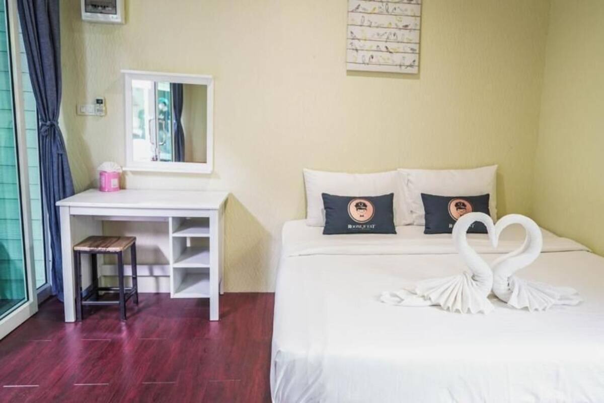 Quarto de hotel com uma cama, uma escrivaninha e uma cadeira. Há um espelho sobre a escrivaninha e uma decoração na parede acima da cama.