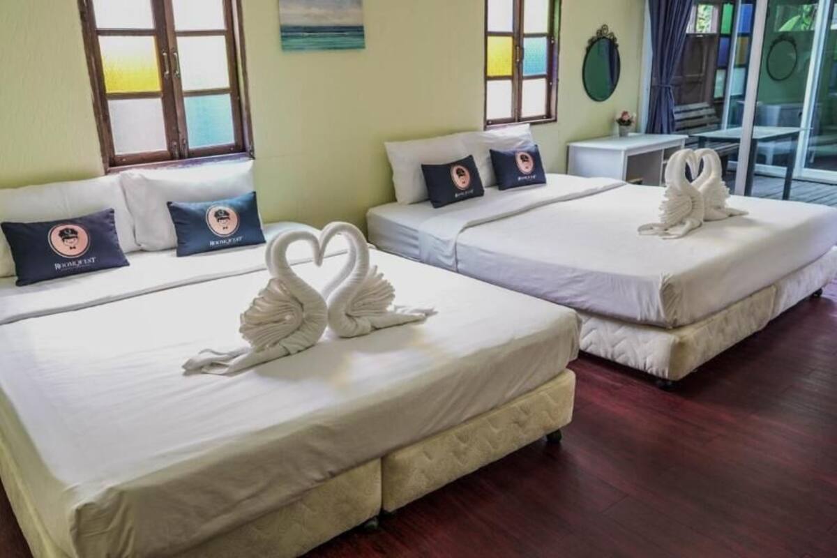 Quarto de hotel com duas camas, cada uma decorada com uma toalha em formato de coração, uma pequena mesa de trabalho e vista para o mar pela janela.