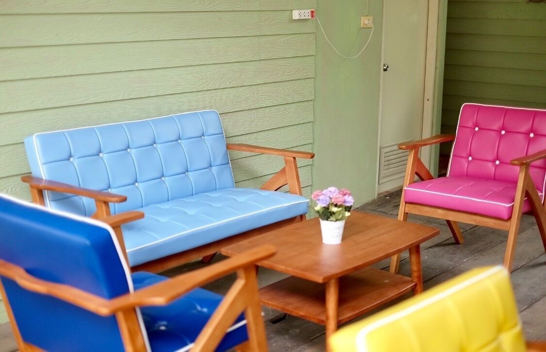 Un conjunto de tres sillas y una mesita con un florero, situados frente a una pared verde.