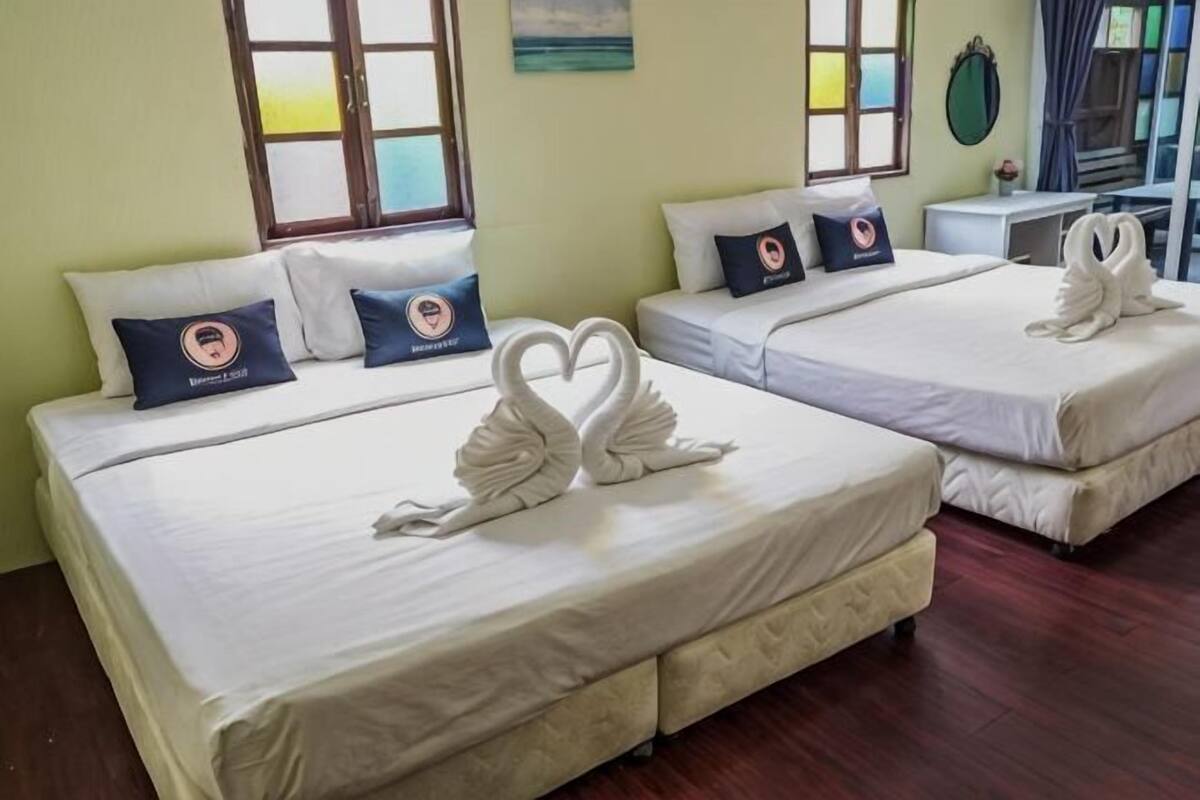 Quarto de hotel com duas camas, cada uma com arrumação de toalhas em formato de coração, uma secretária pequena e vista para o mar pela janela.