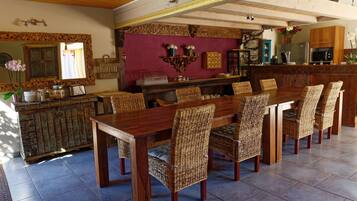 A dining area with a long wooden table and wicker chairs, a kitchen in the background, and a decorative mirror above the table.