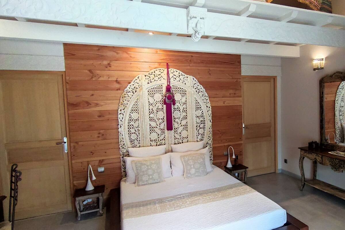 A bedroom with a large bed, wooden panel walls, a mirror, and a small bedside table.
