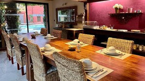 Un comedor con una larga mesa de madera dispuesta para una comida, sillas de mimbre y una pared roja decorativa.