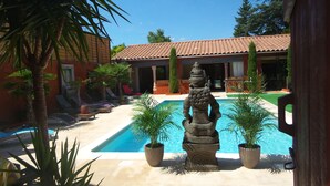 A pool area with a stone sculpture, palm trees, and lounge chairs. - Couleurs du Sud Chambres d'Hôtes (Vallon-Pont-d'Arc)