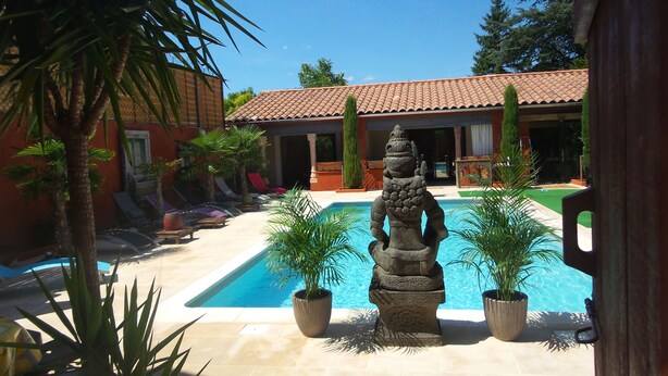 Un área de piscina con una escultura de piedra, palmeras y sillones de descanso.