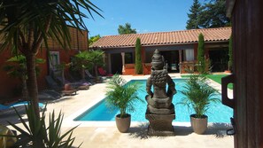 Un área de piscina con una escultura de piedra, palmeras y sillones de descanso.