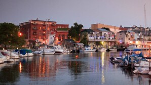 Marina con barcos amarrados, edificios frente al agua y una superficie acuática tranquila que refleja luces.