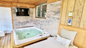 Una habitación acogedora con techo de madera, pared de piedra, televisor grande, bañera y cama con almohada.
