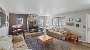 A living room with a stone fireplace, beige sofas, a wooden coffee table, and a fireplace screen. - Fireplace nights, starry skies, wildlife mornings! (Parks)