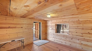 A wooden cabin interior with a bench, a door leading outside, and a window with a view of trees. - Fireplace nights, starry skies, wildlife mornings! (Parks)