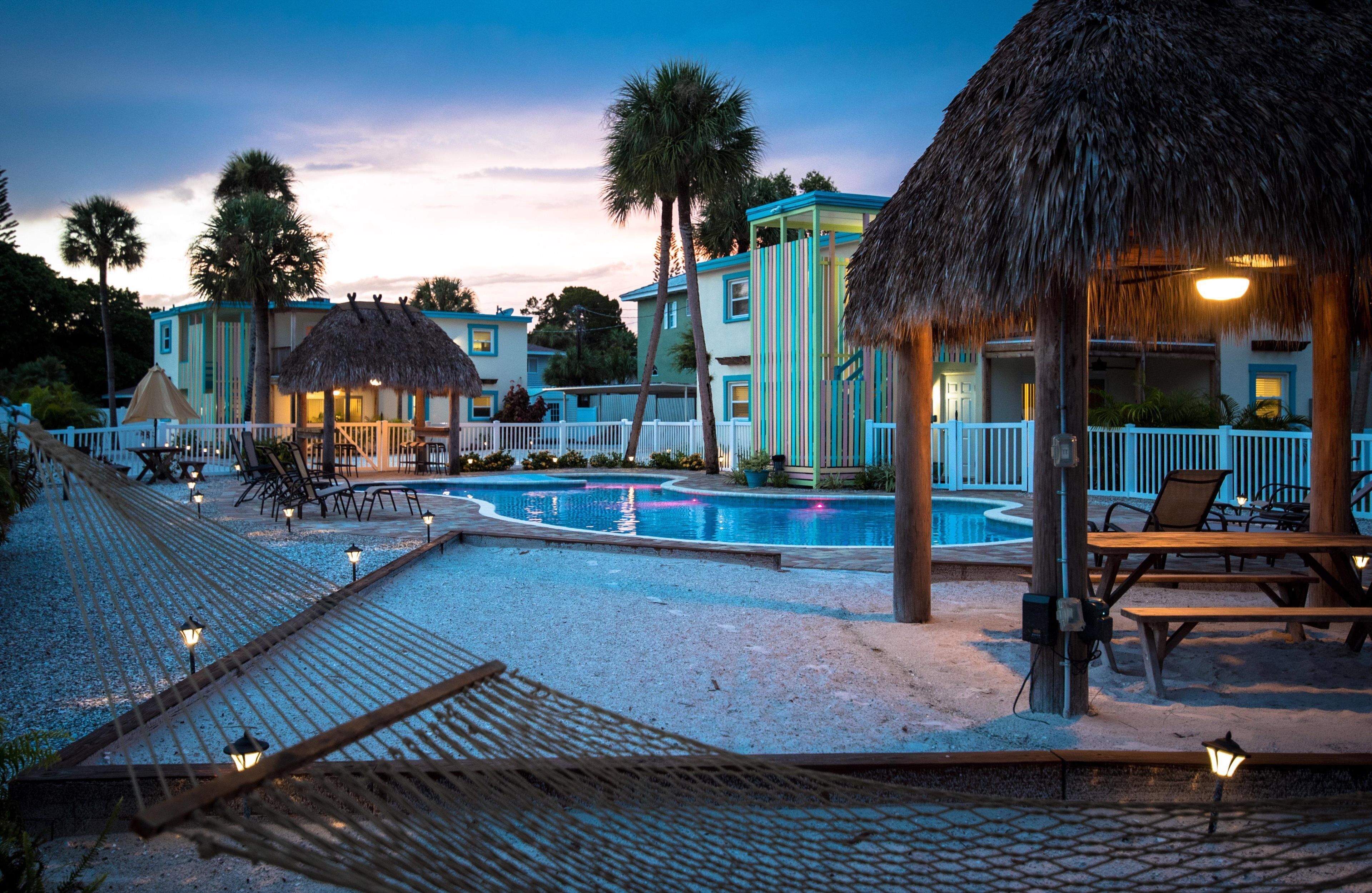 Een resort met een zwembad, rieten dakgebouwen en buitenzitplaatsen.