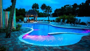A swimming pool with a thatched-roof gazebo, lounge chairs, and palm trees. - Centrally Located Condo with Amazing Pool a Block from SK Village, Pet Friendly (Sarasota)