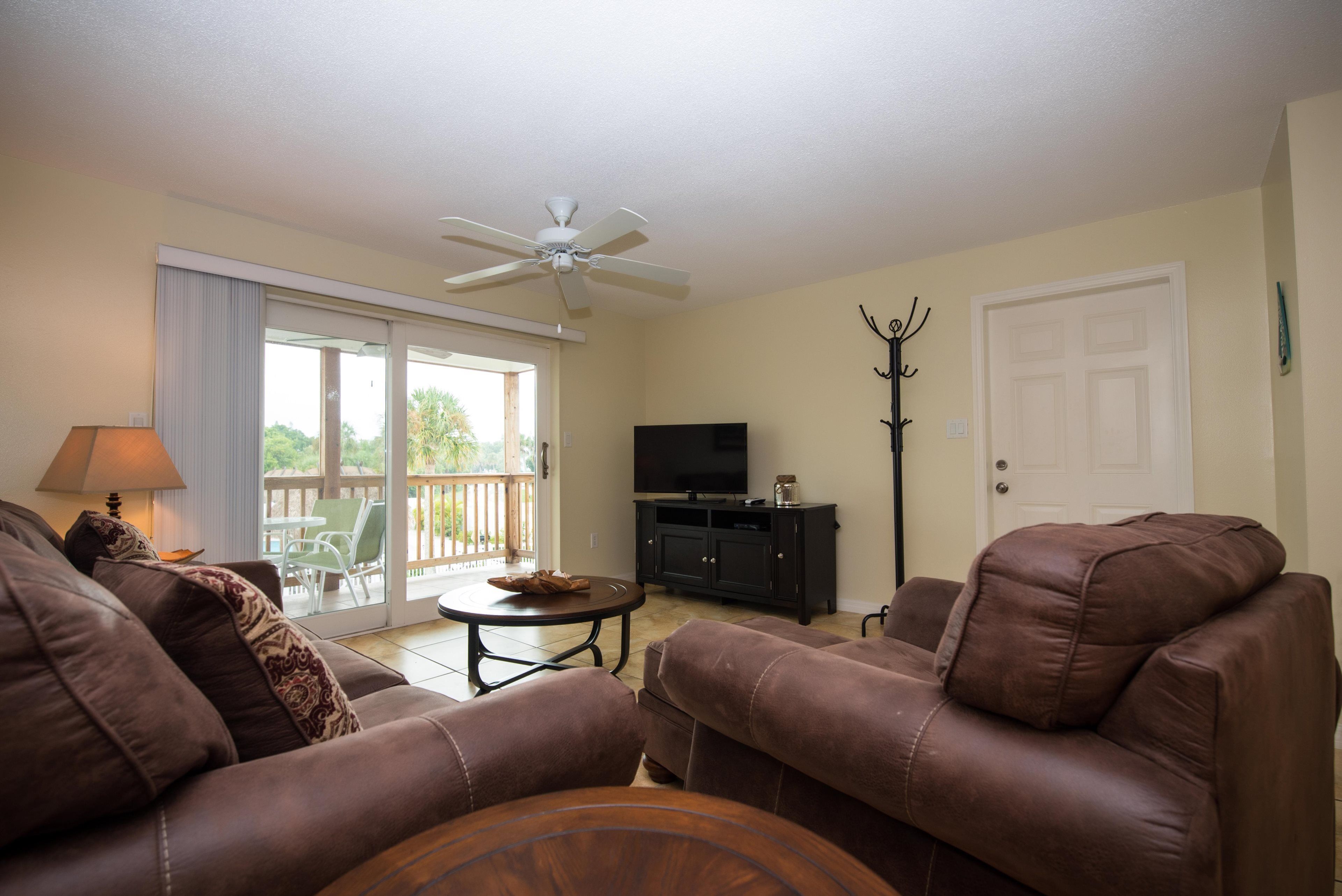 A living room with brown leather sofas, a television on a black cabinet, and a ceiling fan.