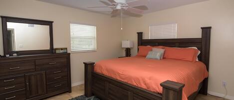 Un dormitorio con una cama de madera, un aparador, un ventilador de techo y dos ventanas con persianas.