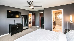 A bedroom with a bed, a dresser, a TV, a ceiling fan, and a bathroom visible through an open door. - On golf course luxurious 2 bed/2 bath condo in the heart of Scottsdale (Scottsdale)