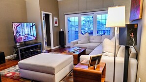 A modern living room with a large window, a television, a sofa, an ottoman, and a coffee table. - On golf course luxurious 2 bed/2 bath condo in the heart of Scottsdale (Scottsdale)