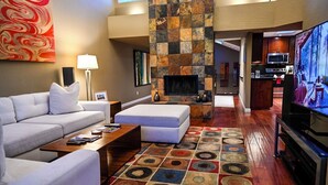 A modern living room with a sofa, ottoman, coffee table, and a TV. There's a fireplace, a kitchen in the background, and a patterned rug. - On golf course luxurious 2 bed/2 bath condo in the heart of Scottsdale (Scottsdale)