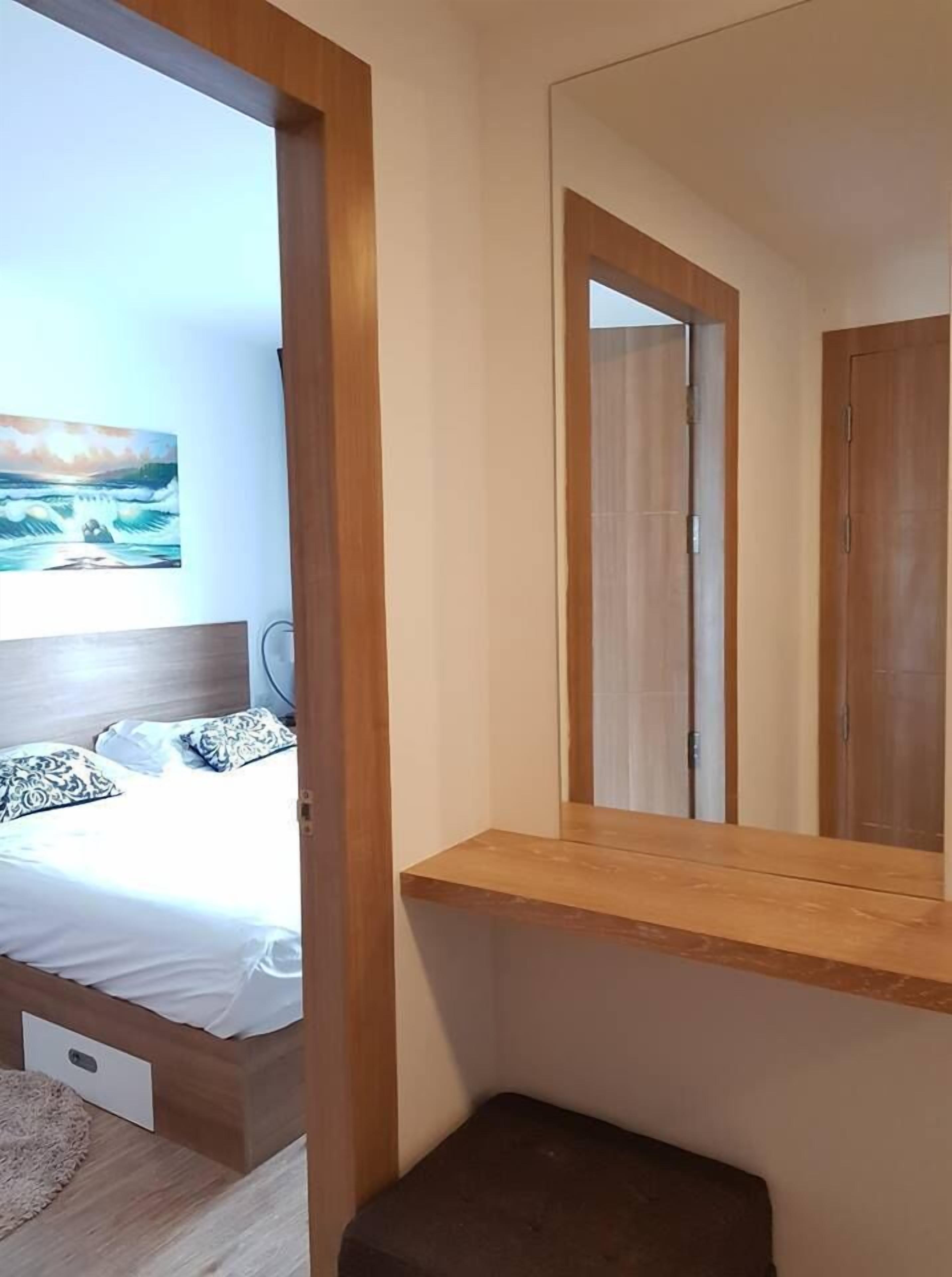 A bedroom with a bed, a nightstand, a mirror, and a painting on the wall.