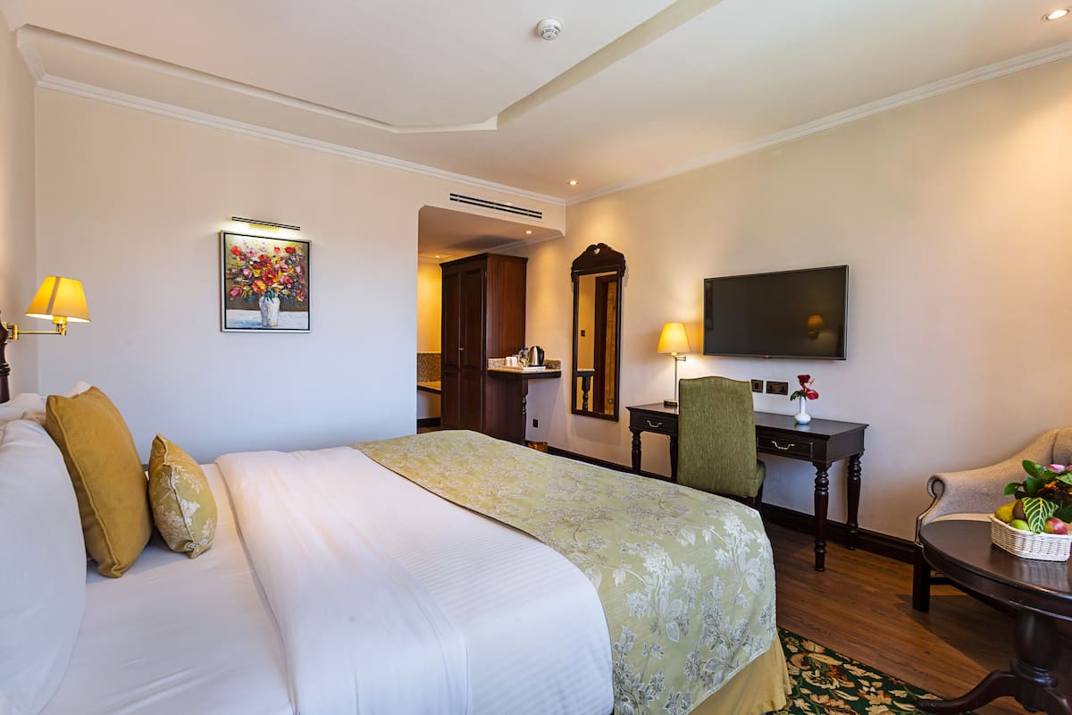 A hotel room with a large bed, a desk, a chair, a television, and a small table with a basket.