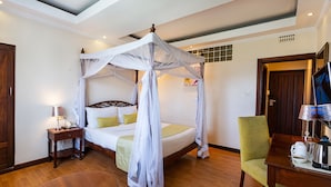 A bedroom with a four-poster bed, a bedside table with a lamp, a green armchair, and a wooden coffee table.