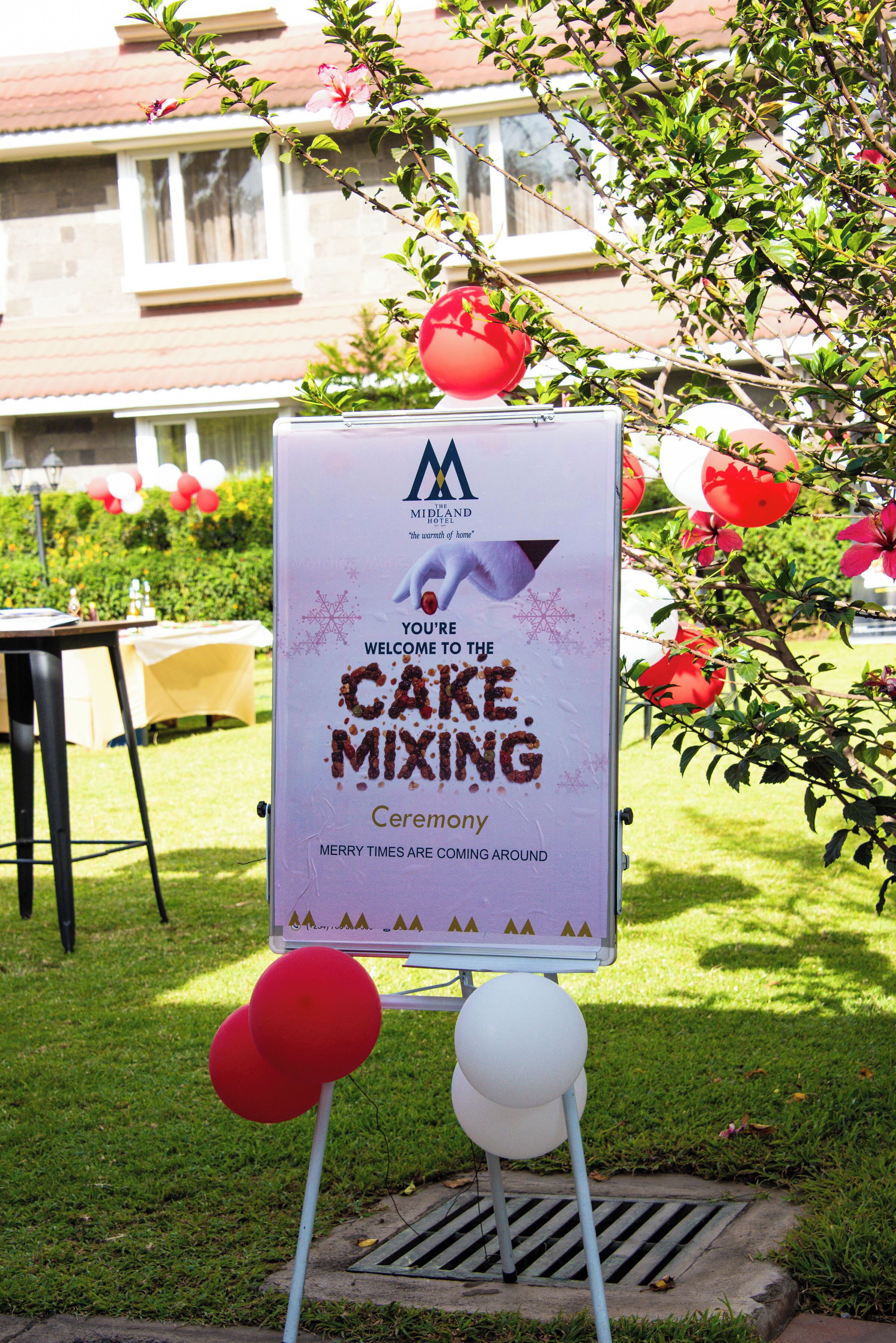 Letrero para una ceremonia de preparación de pastel con globos y un edificio al fondo.