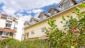 A multi-story residential building with balconies, a red-tiled roof, and a clear sky.