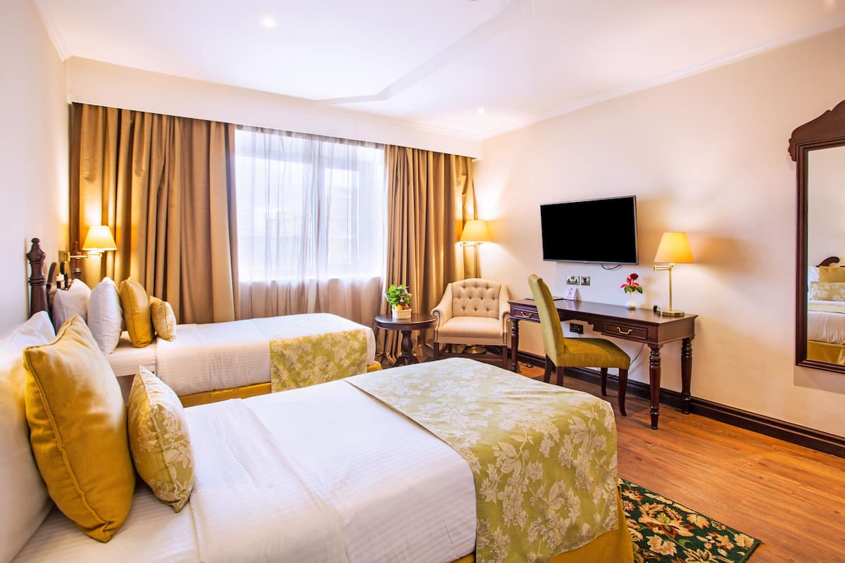 A hotel room with two beds, a desk, a chair, a television, and a large window with curtains.