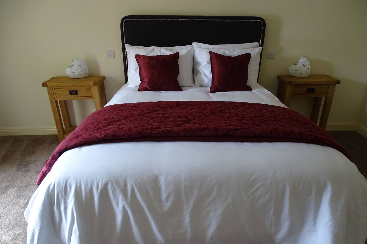 A neatly made bed with white and red bedding, two bedside tables with decorative items, and a wooden headboard.