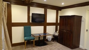 A room with a television mounted on the wall, a wooden cabinet, a teal chair, a small table, and a carpeted floor. - Ellesmere Hotel (Ellesmere)