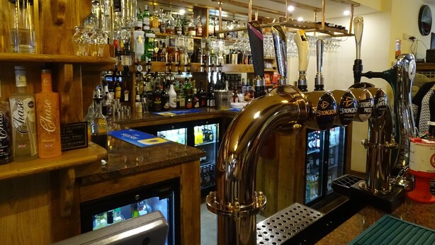 A bar area with multiple taps, shelves of liquor bottles, and a refrigerated display. - Ellesmere Hotel (Ellesmere)
