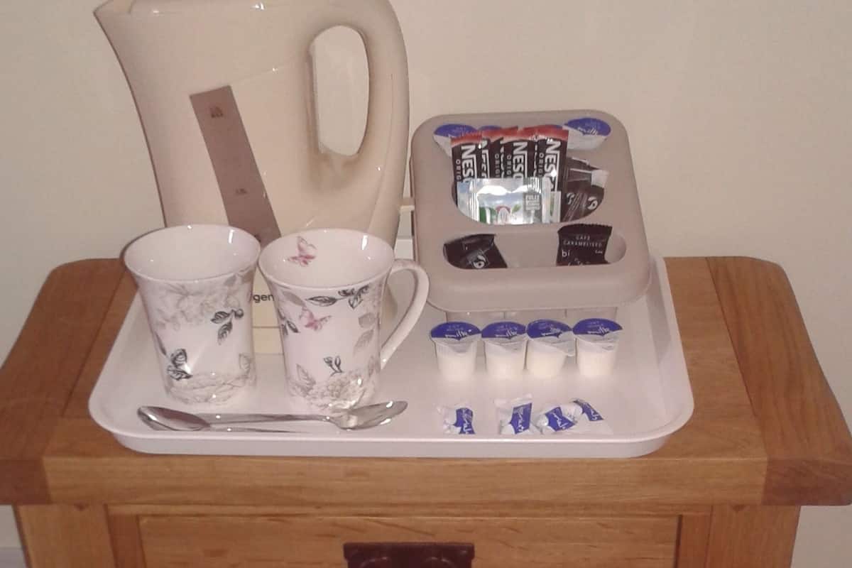 A wooden side table with a tray holding a floral cup, a teapot, a spoon, and a pack of Nescafé instant coffee.