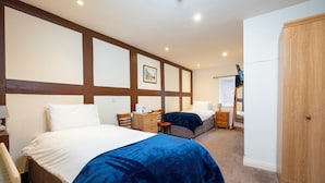 A hotel room with a large bed, a smaller bed, a wooden wardrobe, a desk with a chair, and a nightstand with a lamp. - Ellesmere Hotel (Ellesmere)