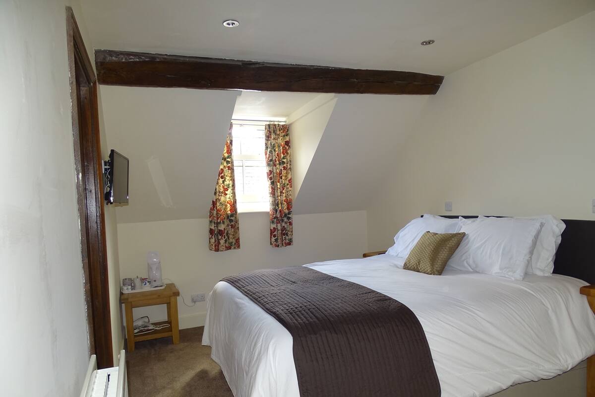 A bedroom with a bed, a nightstand, a window with curtains, and a radiator.