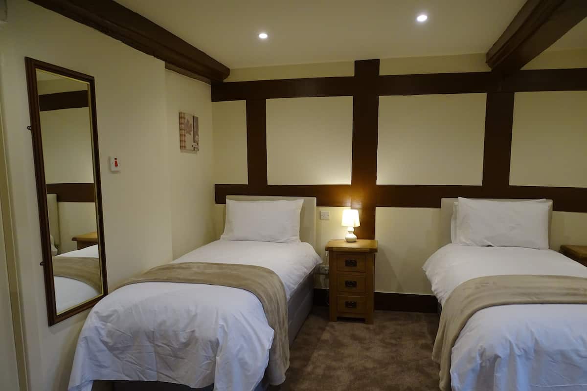 A hotel room with two single beds, a nightstand with a lamp, a mirror, and a wooden headboard.
