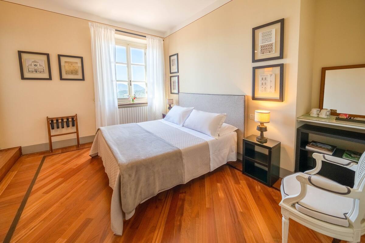 Um quarto bem arrumado com uma cama, uma cadeira, uma mesa de cabeceira e uma estante com livros.
