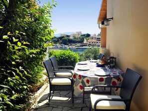 An outdoor dining area with a table set for four, surrounded by wicker chairs, overlooking a scenic view of a coastal town.