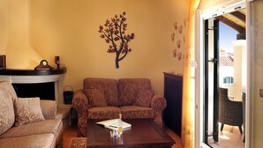 A living room with a sofa, a coffee table, and a fireplace. There is a decorative tree on the wall and a view of the outside through a glass door. - Villa Edem (Corfu)