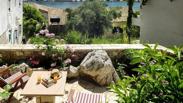 A patio with a table and chairs, overlooking a marina and buildings. - Villa Edem (Corfu)