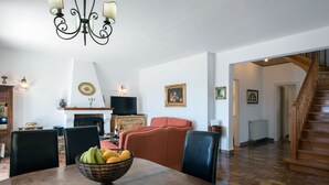 Ein Essbereich mit einem Holztisch, Stühlen, einer Obstschale, einem Kamin und einer Treppe, die zu einer anderen Ebene führt.