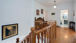Eine Holztreppe führt zu einer zweiten Etage, darüber hängt ein Chandelier und die Wände sind mit Bildern geschmückt.